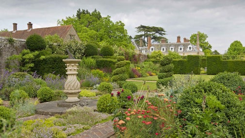 A view of Woolbeding Gardens with a sundial to the left, surrounded by topiary hedges and beds of flowers